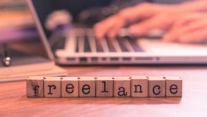 How to Start Your Freelancing Career - block letters spell out freelance while a freelancer works in the background.