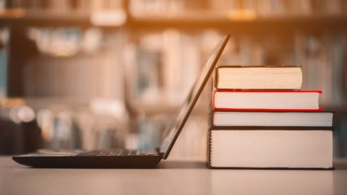 Balancing School and Work Through Remote Jobs - a laptop computer resting against a stack of books in a library.